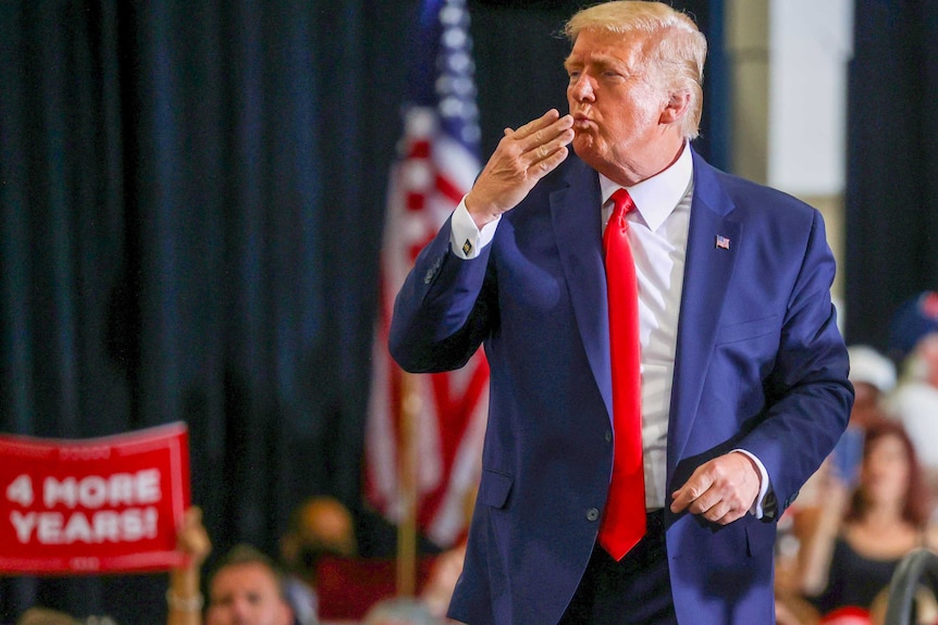 Donald Trump in a red tie and blue suit blowing a kiss