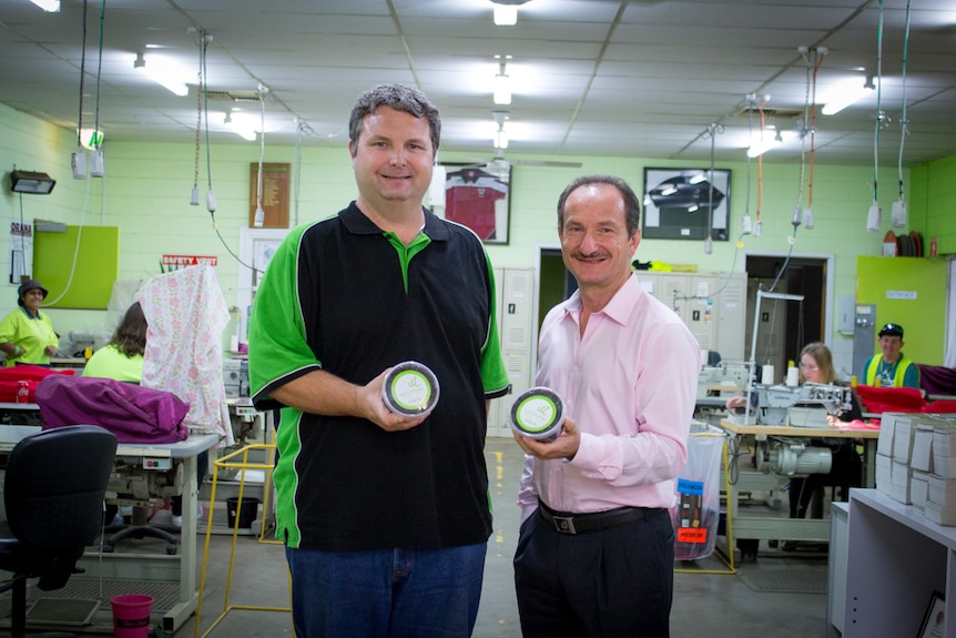 Derek Brown and Nick Mihalaras in a sewing factory holding up tubs with worms for fishing bait.