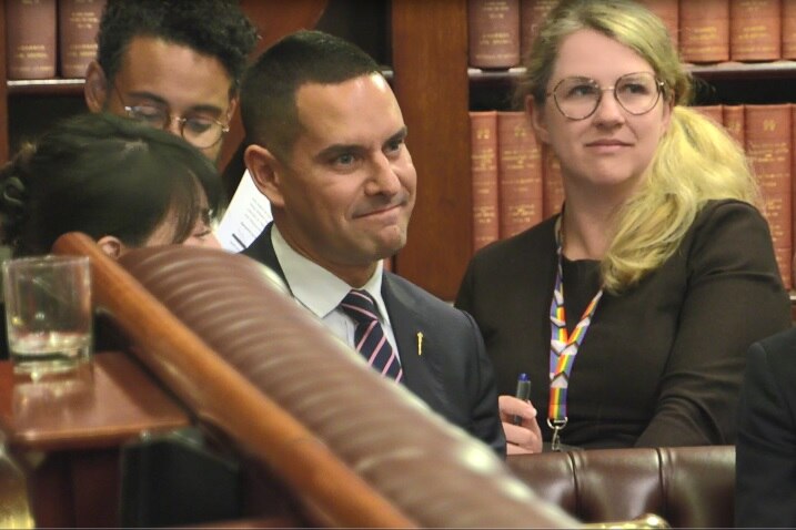 A man in a suit smiles in parliament.