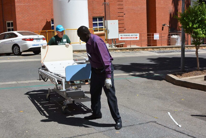 Volunteers wheel a an old RAH bed into a shipping container