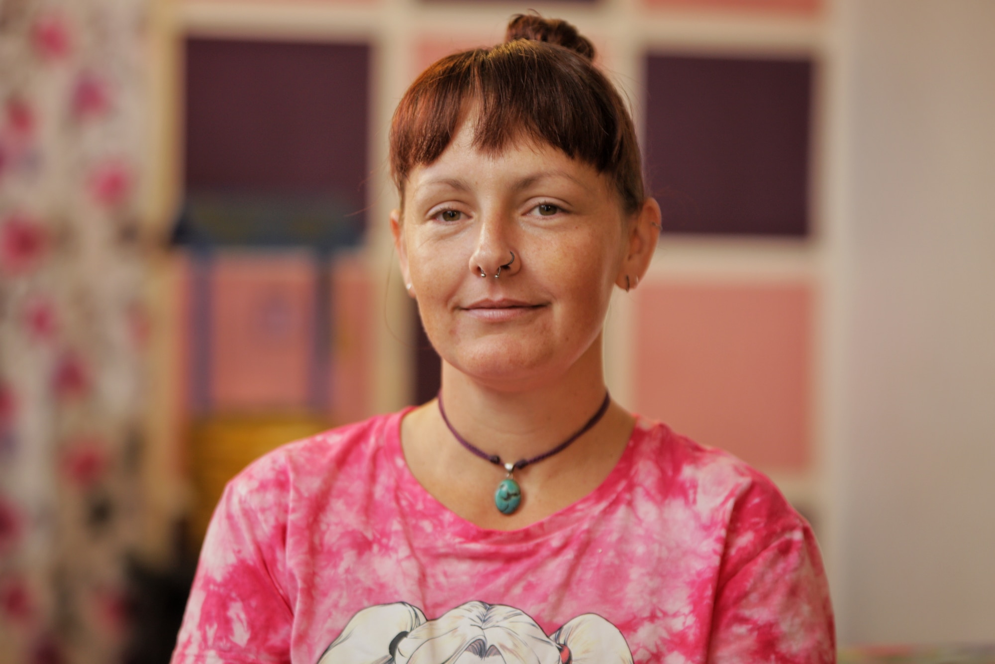 Woman with red hair wearing a bright pink shirt and necklace.