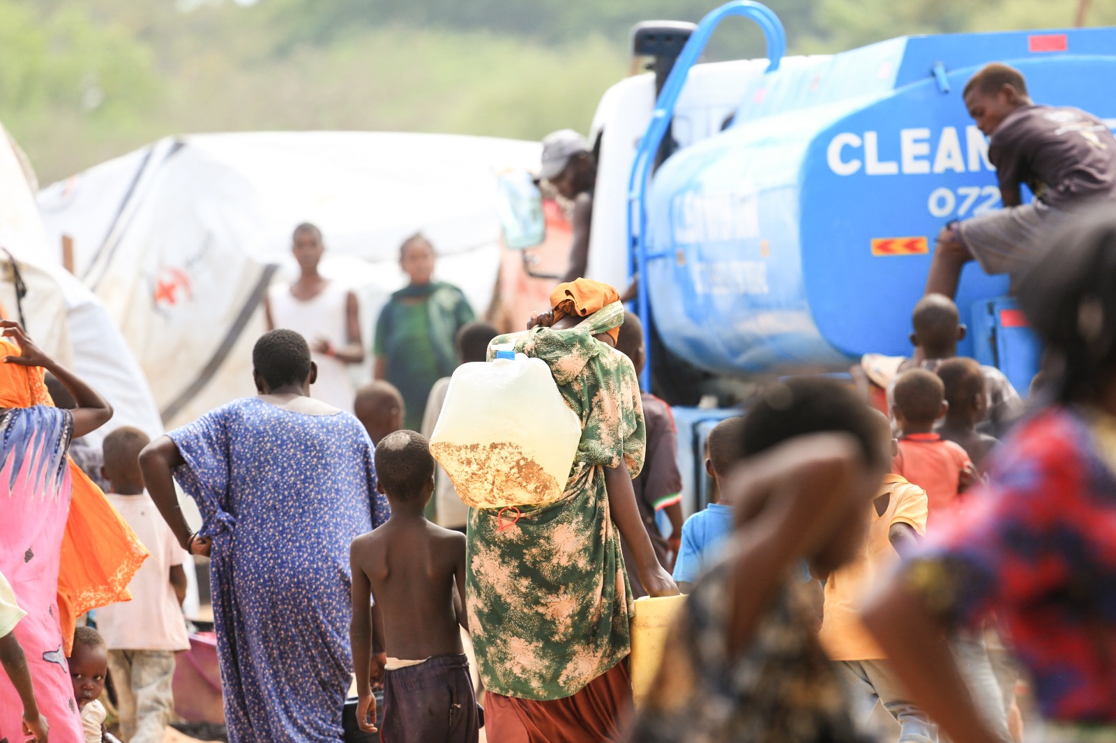 A woman carriers a plastic water jug towards a truck with clean water