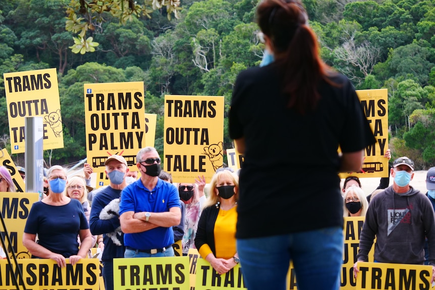 A woman speaks to a crowd of people who are holding protest signs.