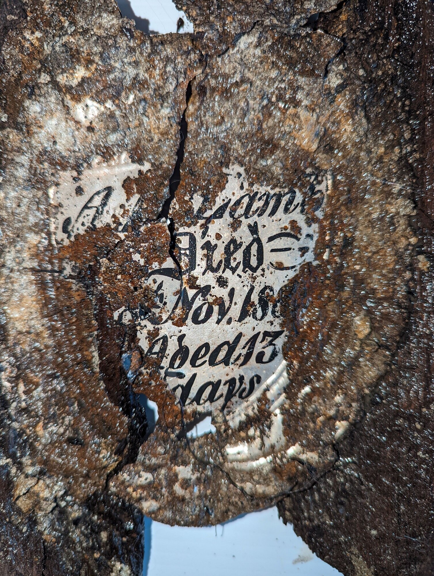 Unreadable coffin nameplate with wording obscured by rust and deterioration.