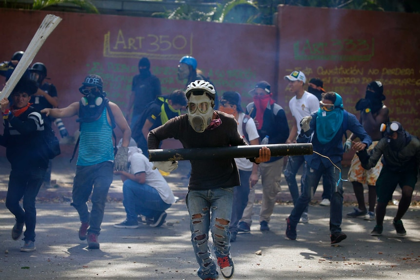 A man wearing a gas mask and bike helmet runs from tear gas holding a homemade mortar.