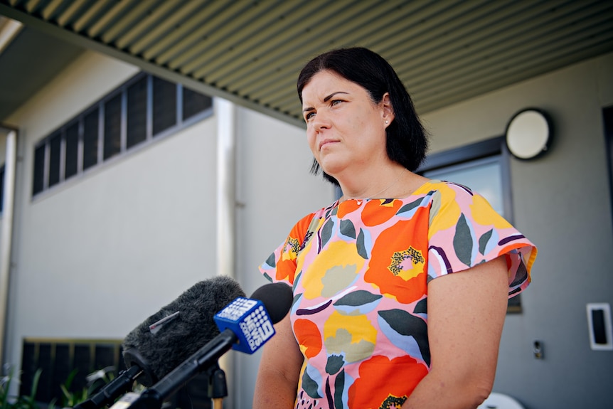 A woman with black hair looks sternly at cameras during a press conference