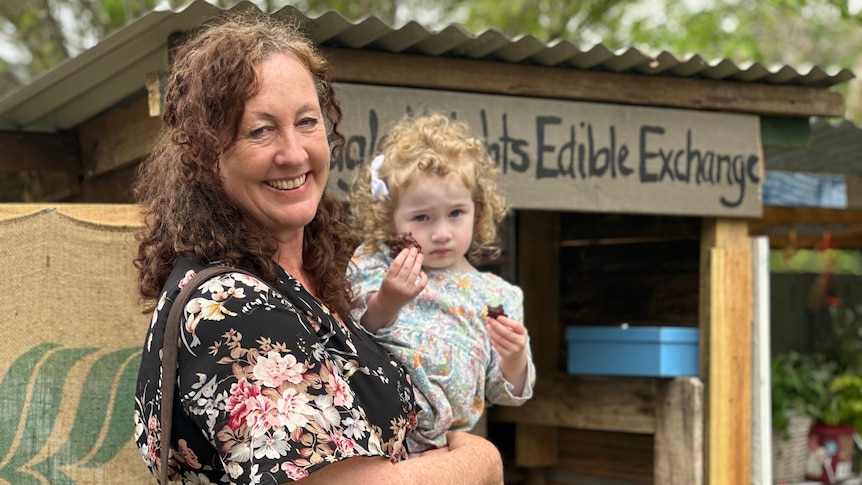 Woman holding a female toddler in front of roadside food exchange stall.