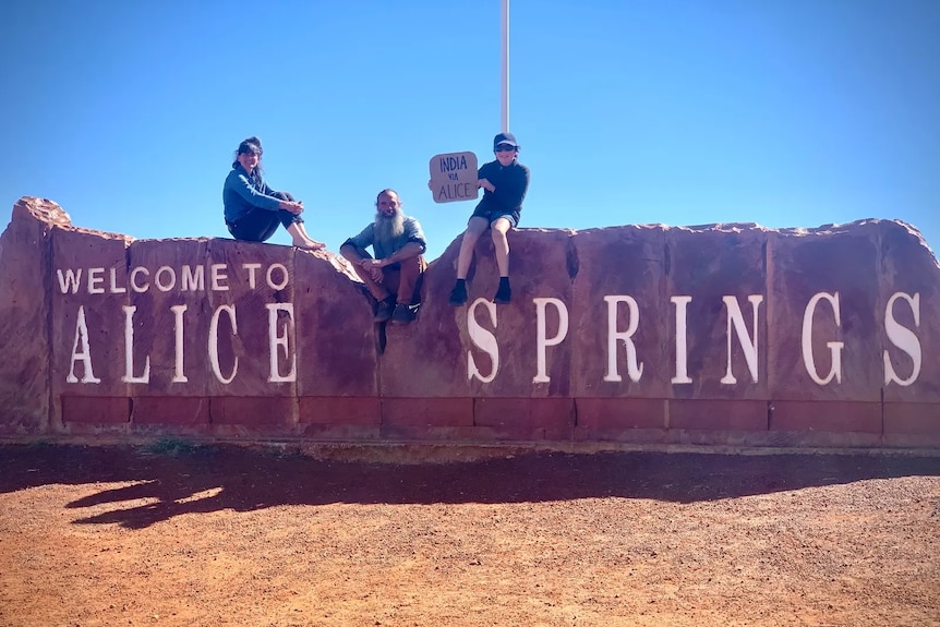 Two adults and a child on a sign saying 'Welcome to Alice Springs'
