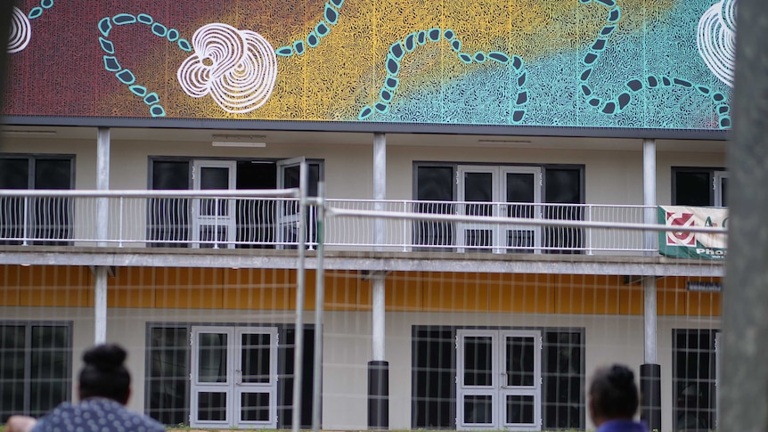 A colourful building including indigenous artwork with a fence and two people in the foreground