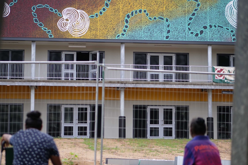 A colourful building including indigenous artwork with a fence and two people in the foreground