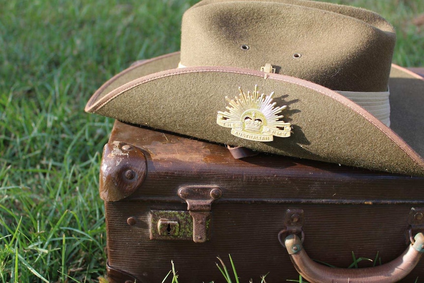 A khaki, wide-brimmed hat. One side is upturned with a gold Australian Army badge on it. The hat is on an old brown suitcase.