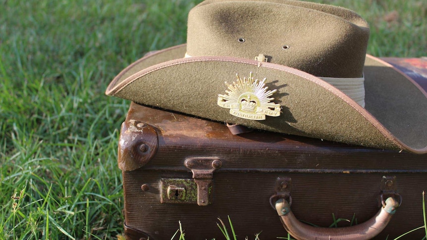 A khaki, wide-brimmed hat. One side is upturned with a gold Australian Army badge on it. The hat is on an old brown suitcase.