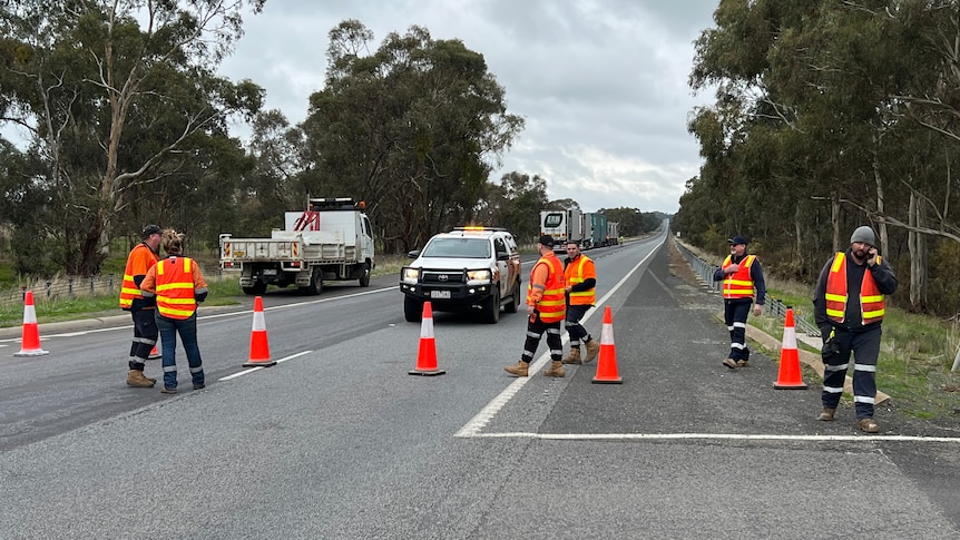 Road workers stand on an empty highway that is cut off with traffic cones