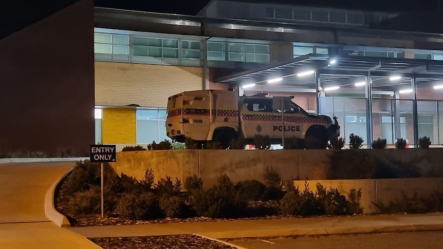 A police car parked outside a hospital emergency department at night. 