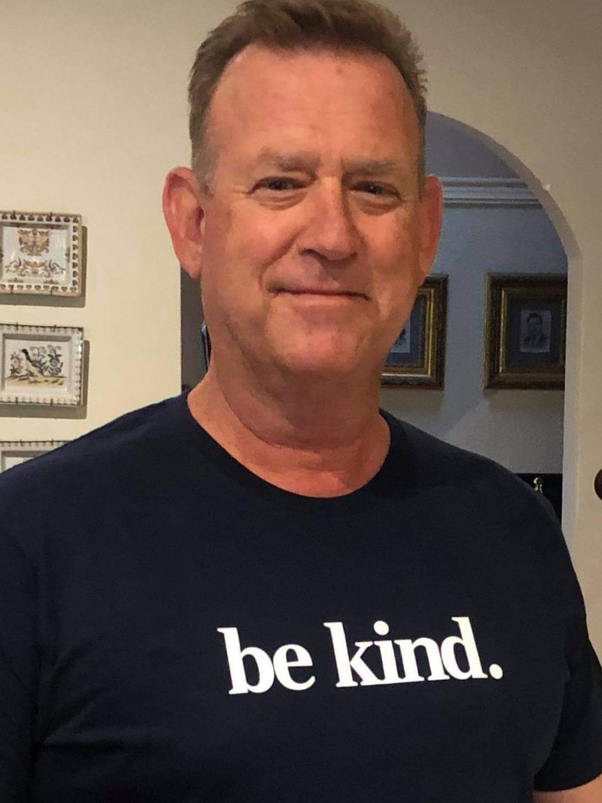 A smiling man with a dark t shirt that reads 'be kind'