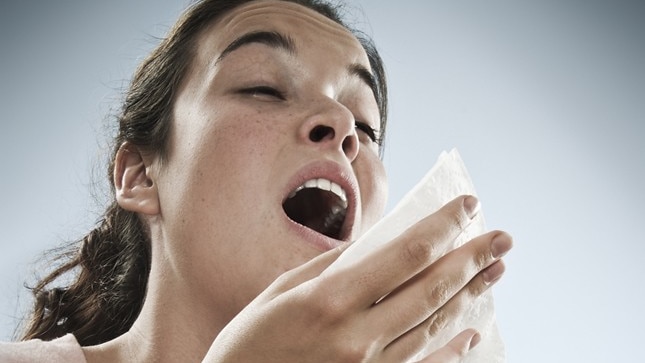 A woman before a sneeze holding a tissue up to her face.