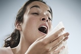 A woman who is just about to sneeze holds a tissue at the ready.