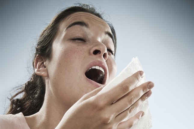 A woman who is just about to sneeze holds a tissue at the ready.