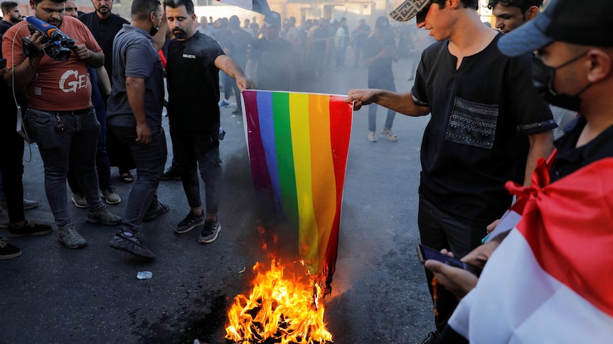 Two men wearing black burn lgbt rainbow flag 