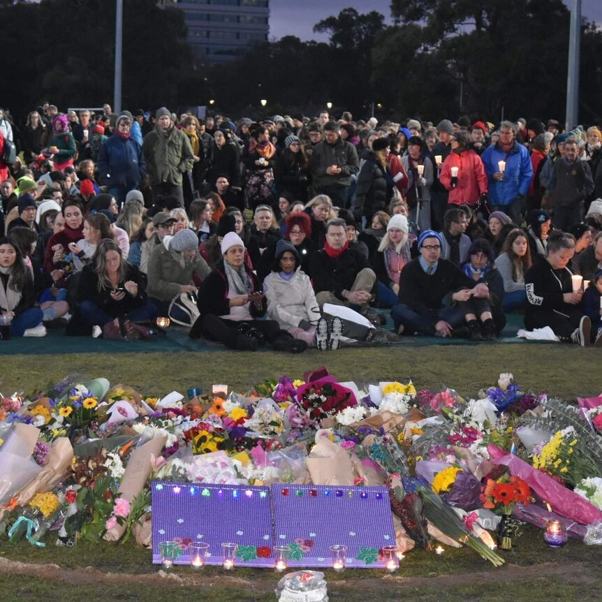 Crowds of people stand and sit in darkness with candles in Princes Park in vigil for Eurydice Dixon.