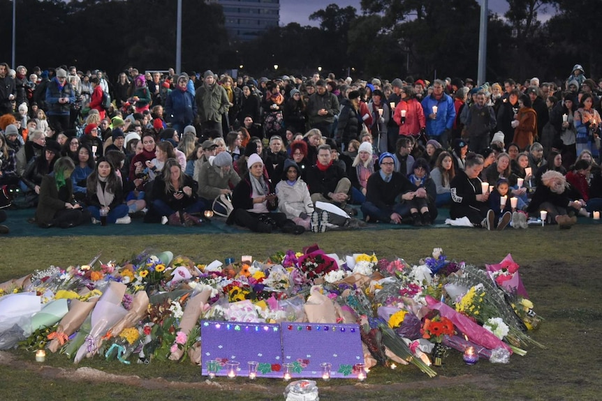 Crowds of people stand and sit in darkness with candles in Princes Park in vigil for Eurydice Dixon.
