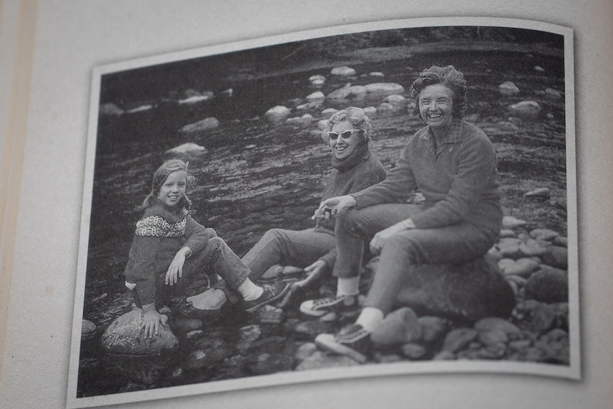 Black and white photo of two women and a young girl sitting on rocks by the water.