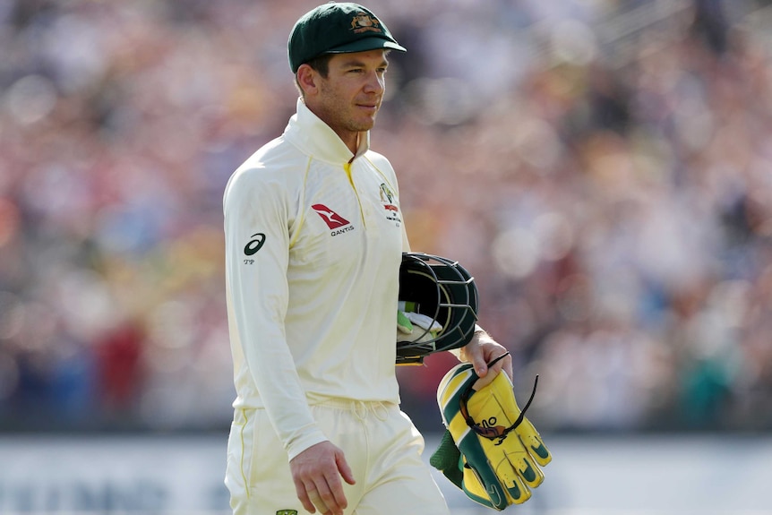 Tim Paine camina con su casco bajo el brazo y guantes de wicketkeeping en la mano.