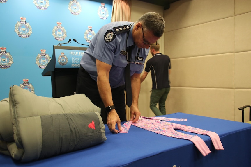 A policeman lays out a child's jumpsuit on a counter