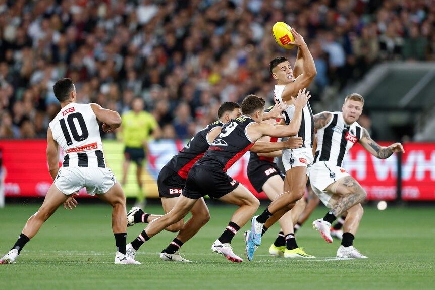 A Collingwood AFL player closes his eyes as he handballs over his head as he is tackled by St Kilda players.