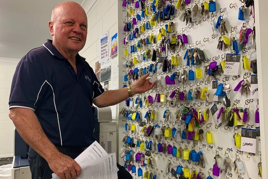A man standing beside a wall of keys hanging on hooks