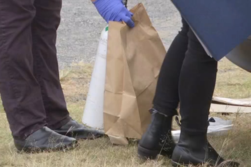 what looks like a white metal object is being put into brown bags by a detective's feet