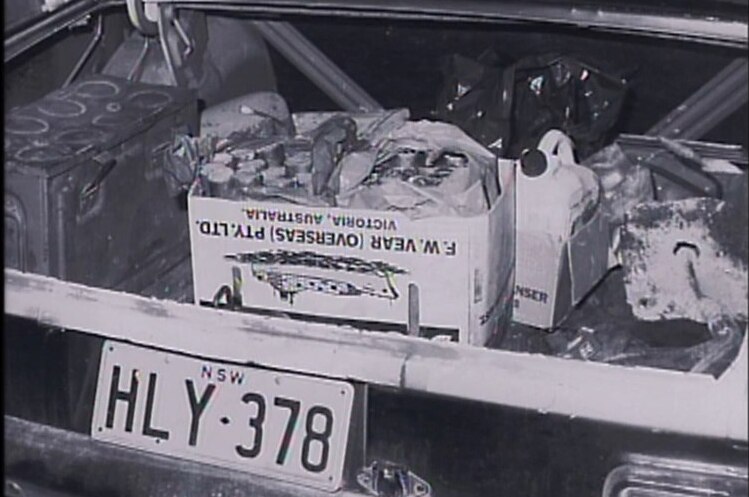 Black and white photograph of an open car boot with boxes of explosives inside.