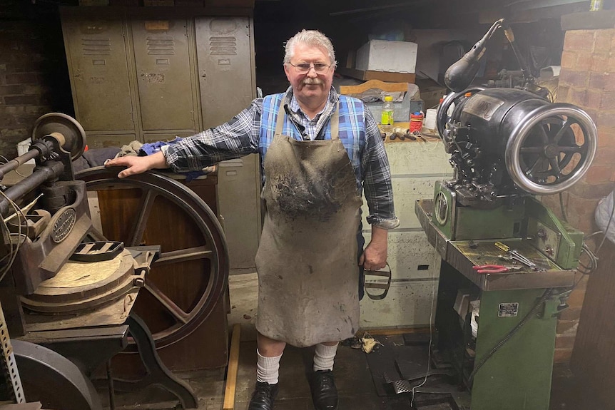 A man wearing an work apron stands among old fashioned machinery.