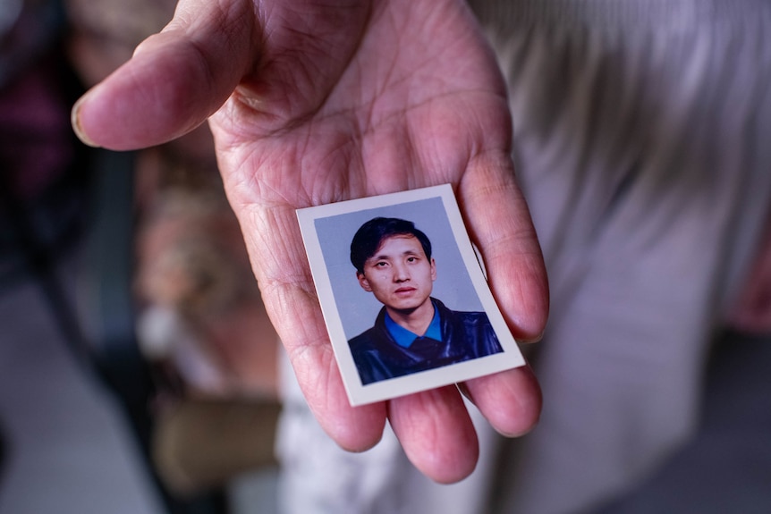 An old man holds a passport photo of a young Chinese man.