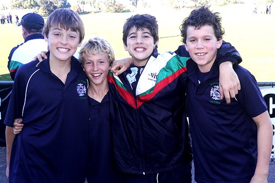 Four junior Australian rules players post for a photograph at a football ground.