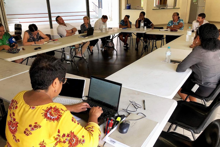 Several staff from Births Deaths and Marriages staff sit at a table with laptops in a hall.