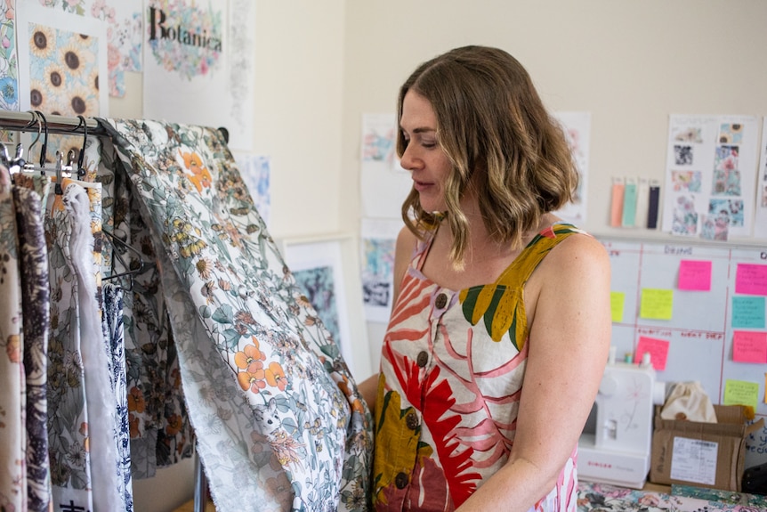 A woman wearing a loose linen dress holds and looks at fabric with an Australiana design.