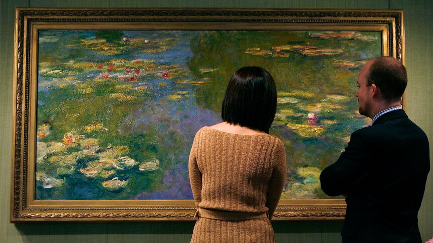 Two people study a Monet water-lily painting in a New York exhibition.