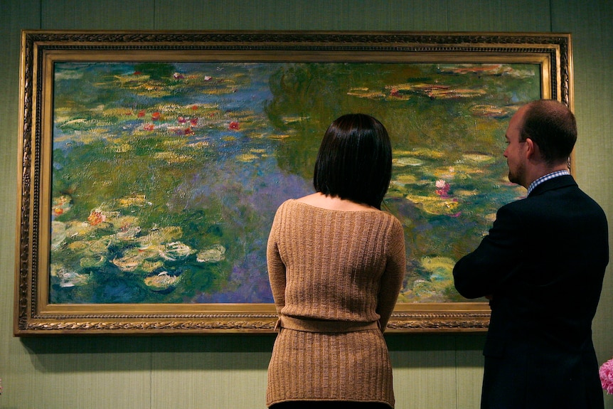 Two people study a Monet water-lily painting in a New York exhibition.