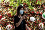 A woman in a face mask texts as she walks past a Christmas treet