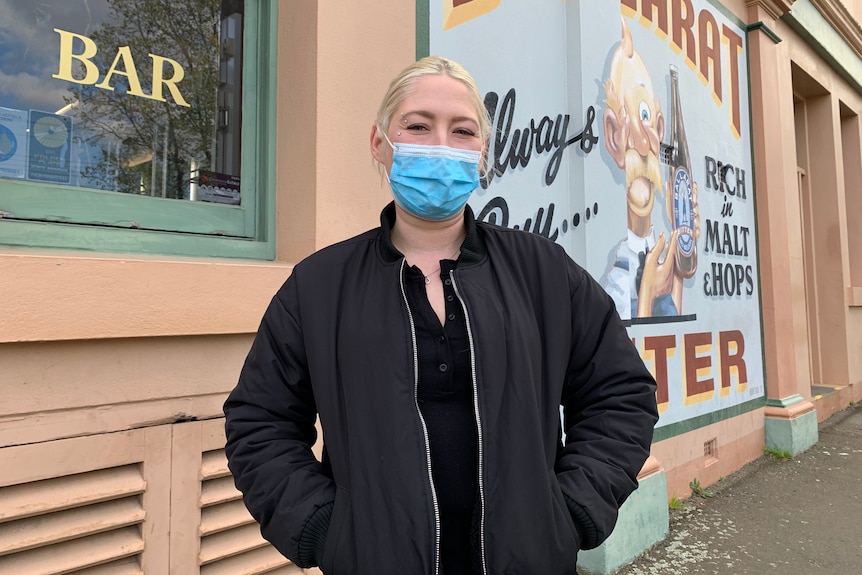 woman in mask looking at the camera with pub in the background