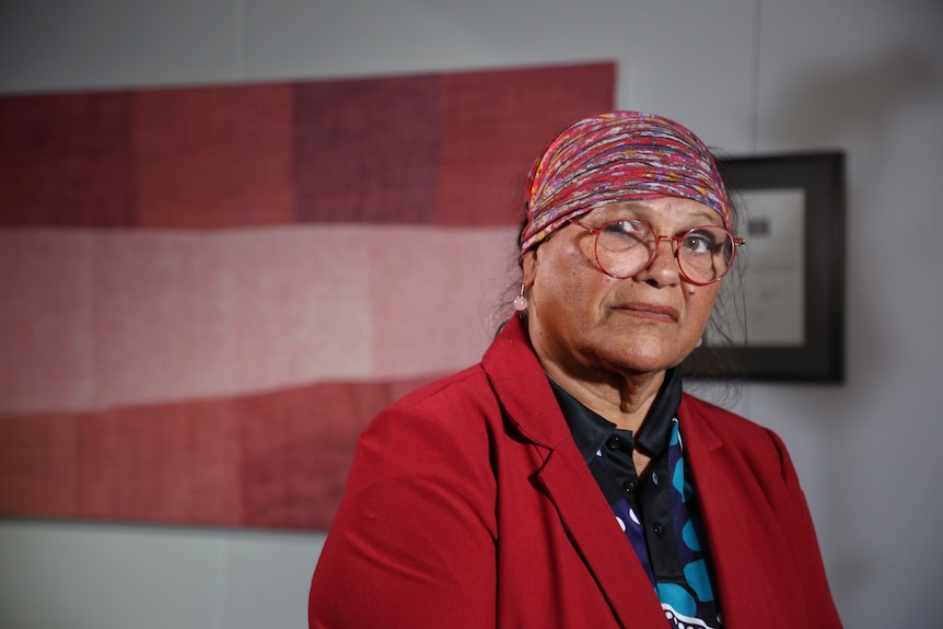 An Indigenous woman in a red headscarf wears a look of concern.