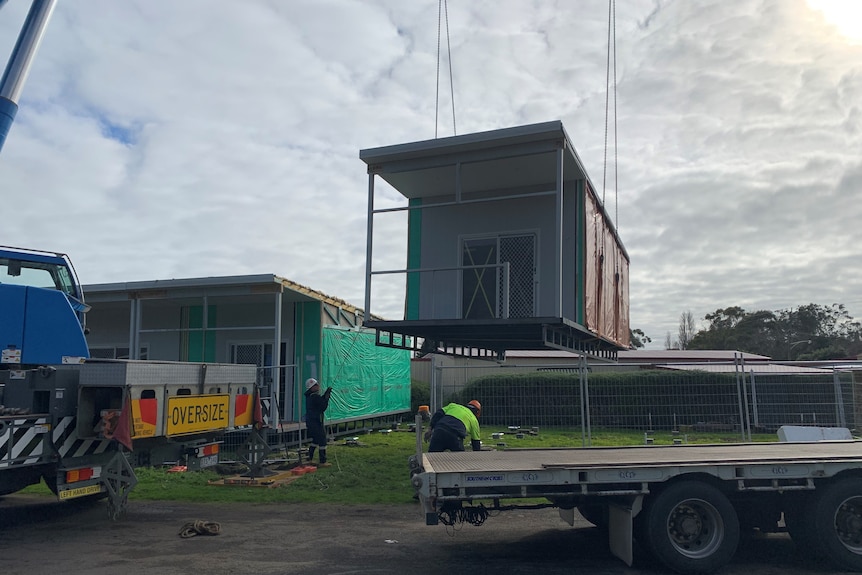 Workers lower a prefabricated cabin into place using a crane.