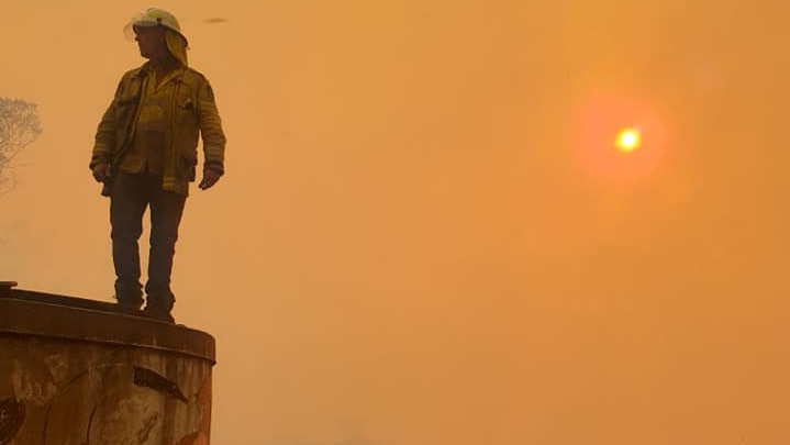 A firefighter in Ewingar stands atop a water tower to survey the scene