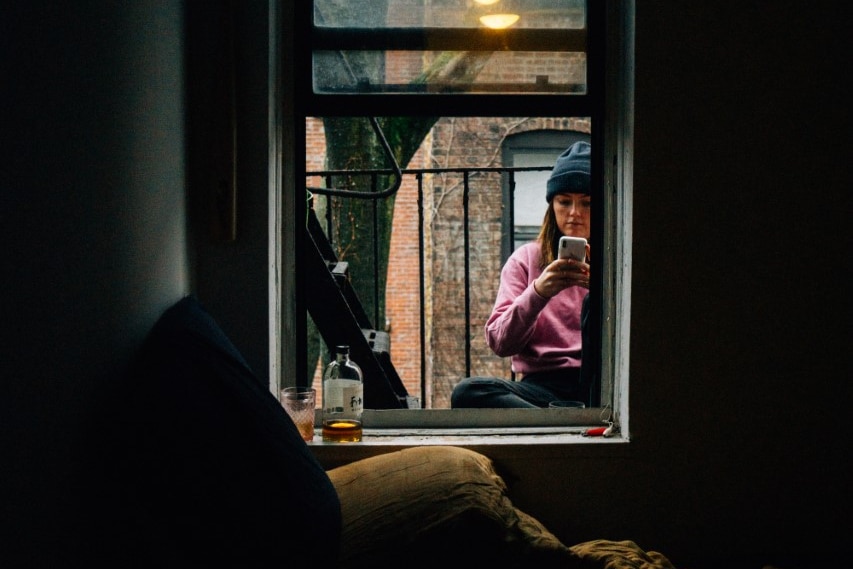 A woman sits outside the window of a small dark apartment 