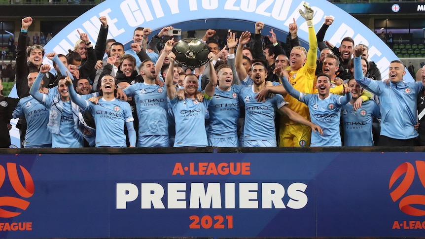 Melbourne City players celebrate while holding up the A-League premiership plate.