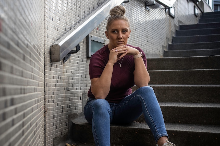 Woman in jeans, maroon top and white sneakers sitting down on stairs.