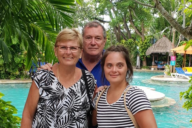 Mother and father with grown daughter beside a resort swimming pool.