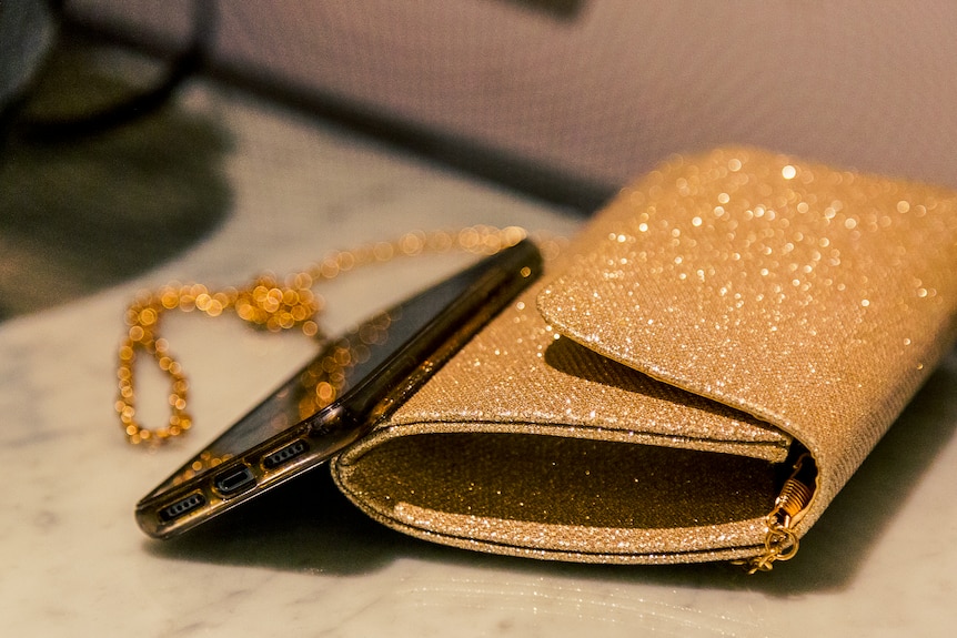 A close-up of a sparkly gold purse and a phone.