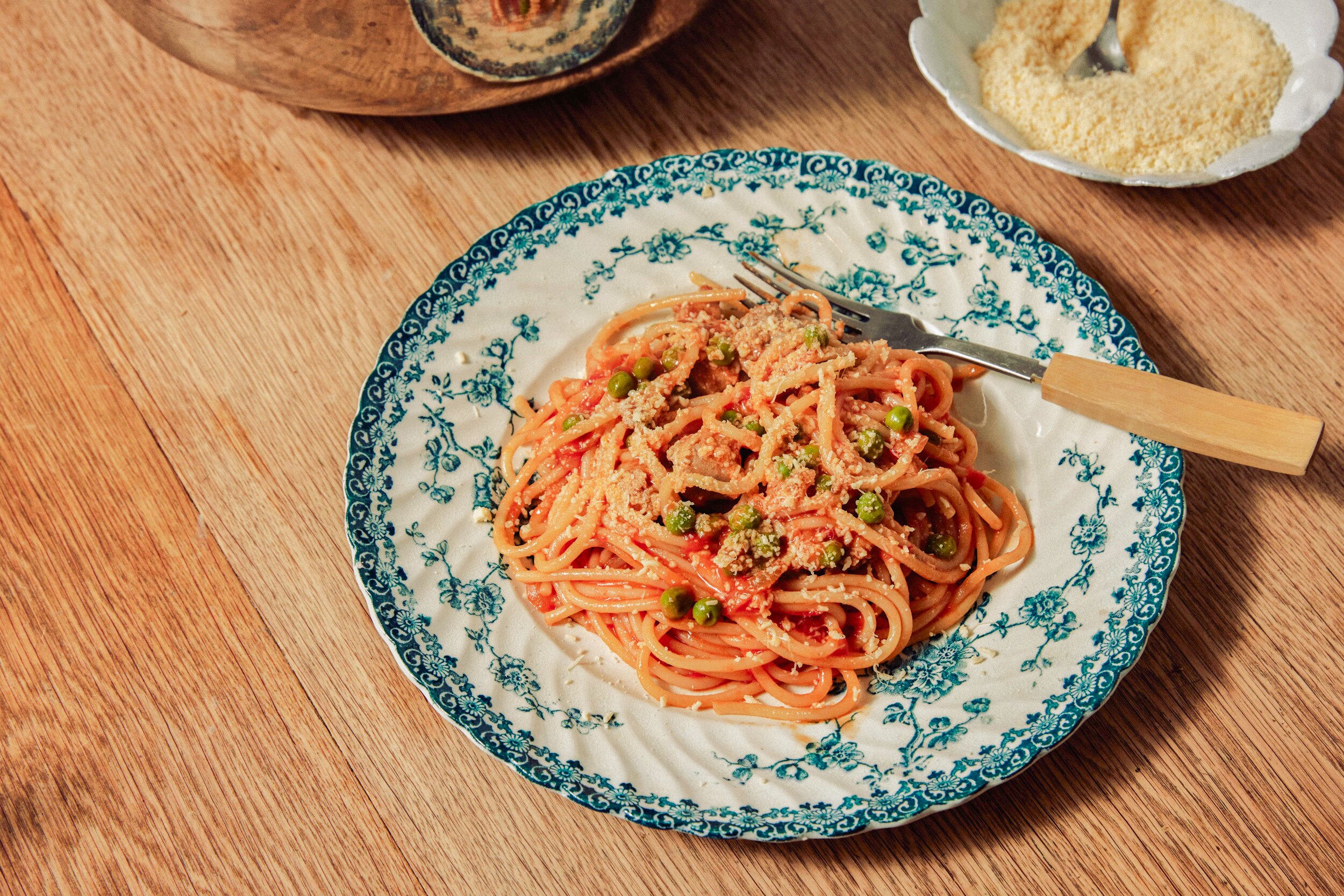 A plate of tomato, sausage and pea spaghetti topped with Parmesan cheese, a cheap and delicious weeknight pasta.